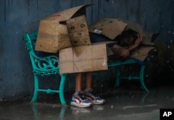 Personas en una parada de autobús se protegen con cartones del viento y la lluvia durante el paso del huracán Rafael en La Habana, Cuba, el miércoles 6 de noviembre de 2024. (Foto AP/Ramon Espinosa)